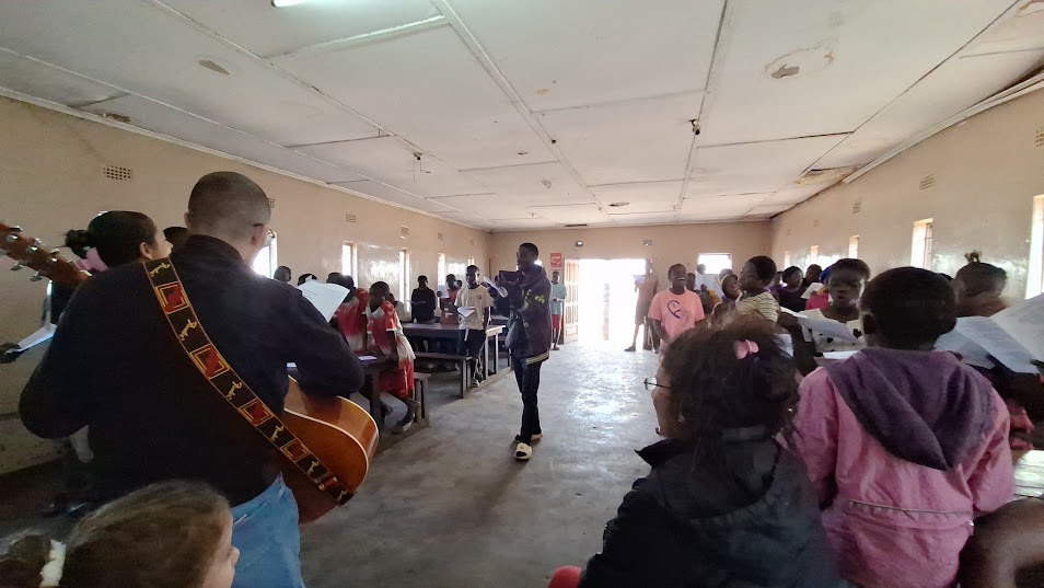The team leading songs with a guitar in a hall full of children holding song sheets